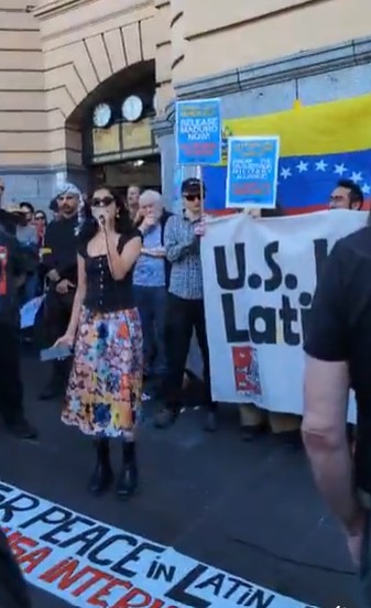 Nandini holding microphone in front of banners at Flinders St