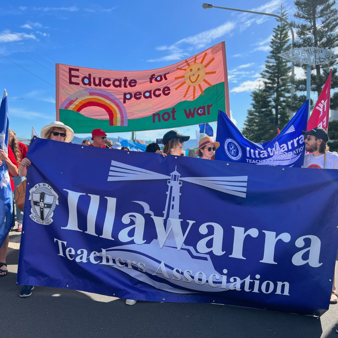 People holding up "Educate for Peace" Banner with a rainbow on it, being held behind an Illawarra Teachers Association branch banner
